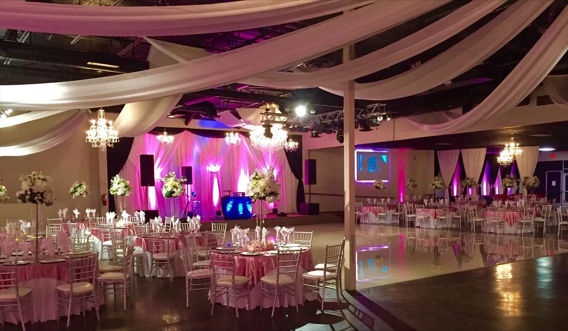 Elegant banquet hall with pink-purple lighting, draped ceiling fabric, and set tables and chairs for an event