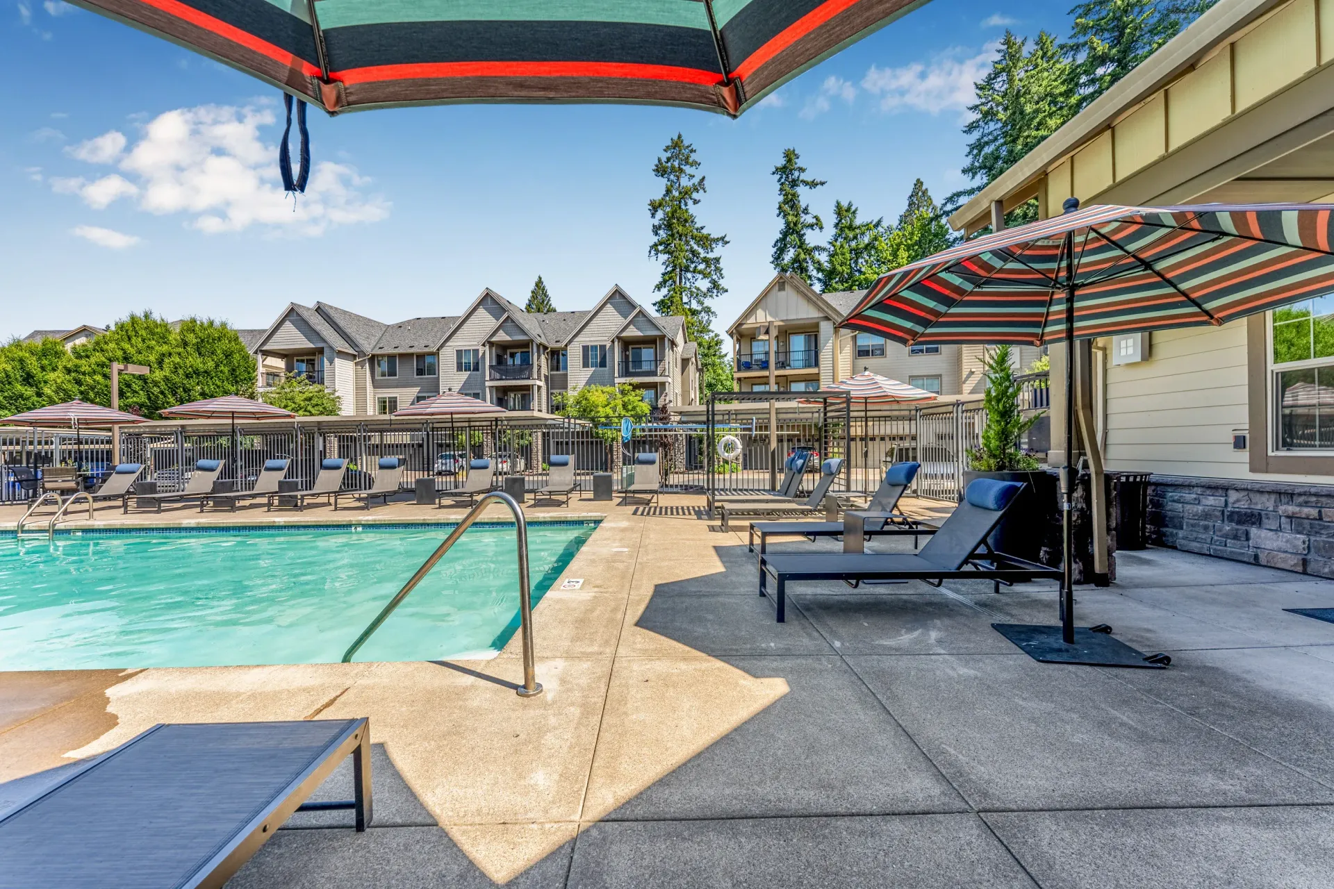 Outdoor apartment pool area with lounge chairs and striped umbrellas.