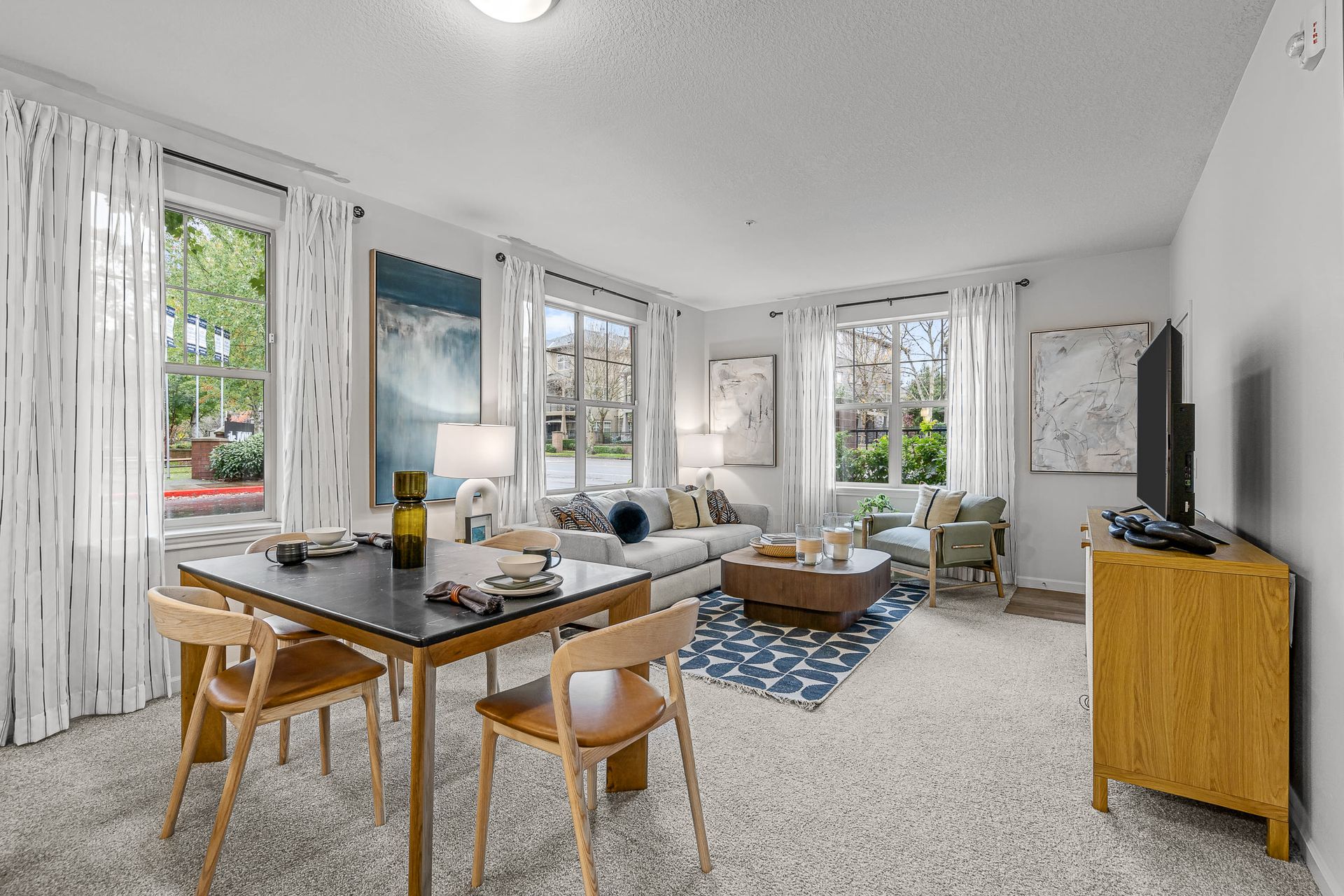 Open living room and dining area in an apartment with a sofa, coffee table, dining table, and TV.