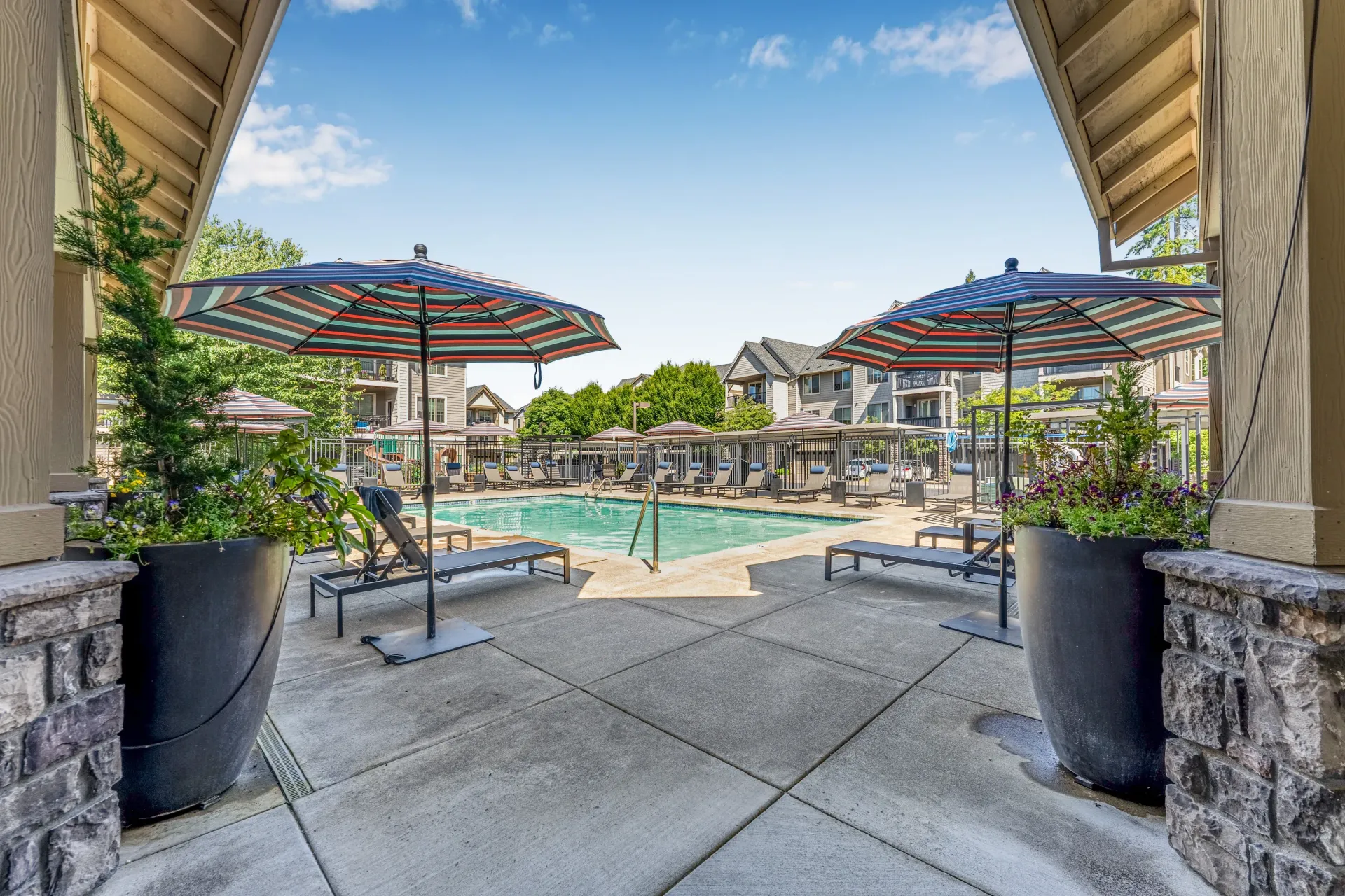 Outdoor apartment community pool area with striped umbrellas and lounge chairs.