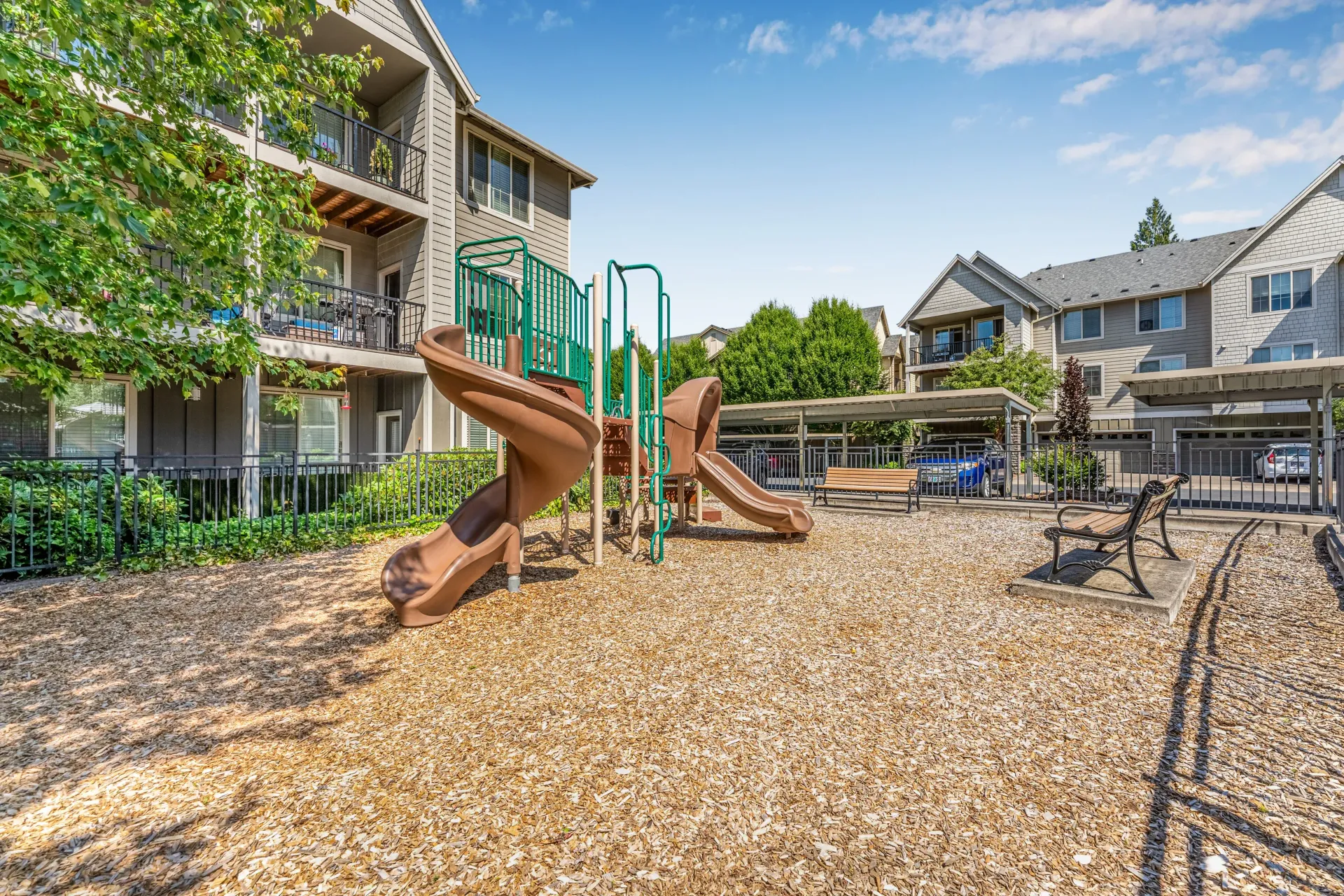 Outdoor playground with brown spiral slide and green railings at apartment community.