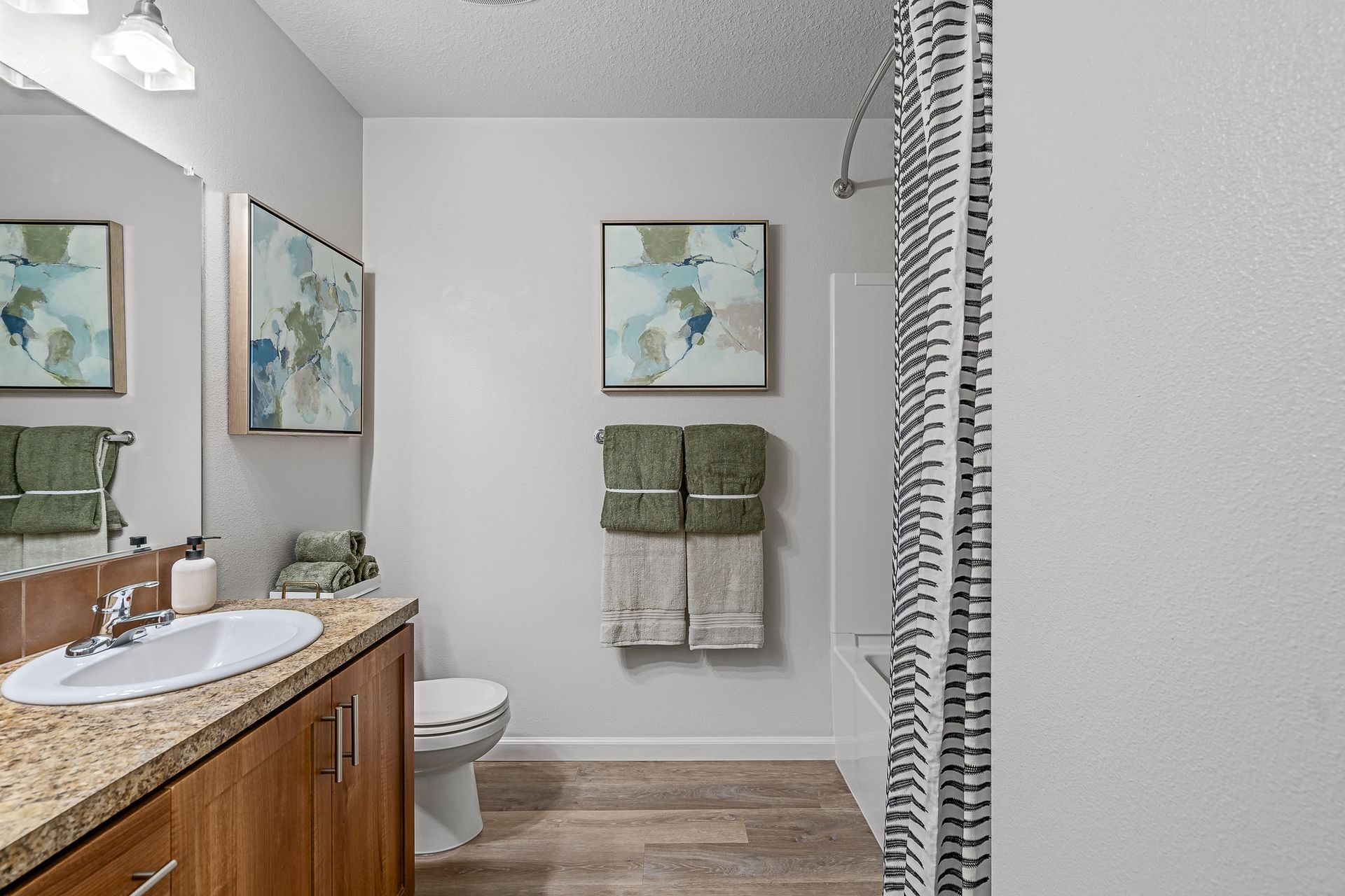 Apartment bathroom with vanity, sink, mirror, toilet, tub/shower, striped curtain, and green towels.