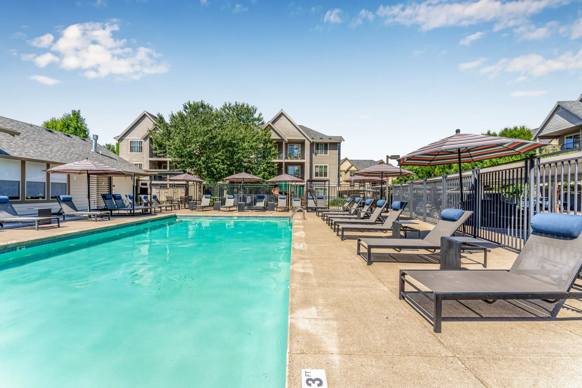 Outdoor apartment community pool with lounge chairs and striped umbrellas.