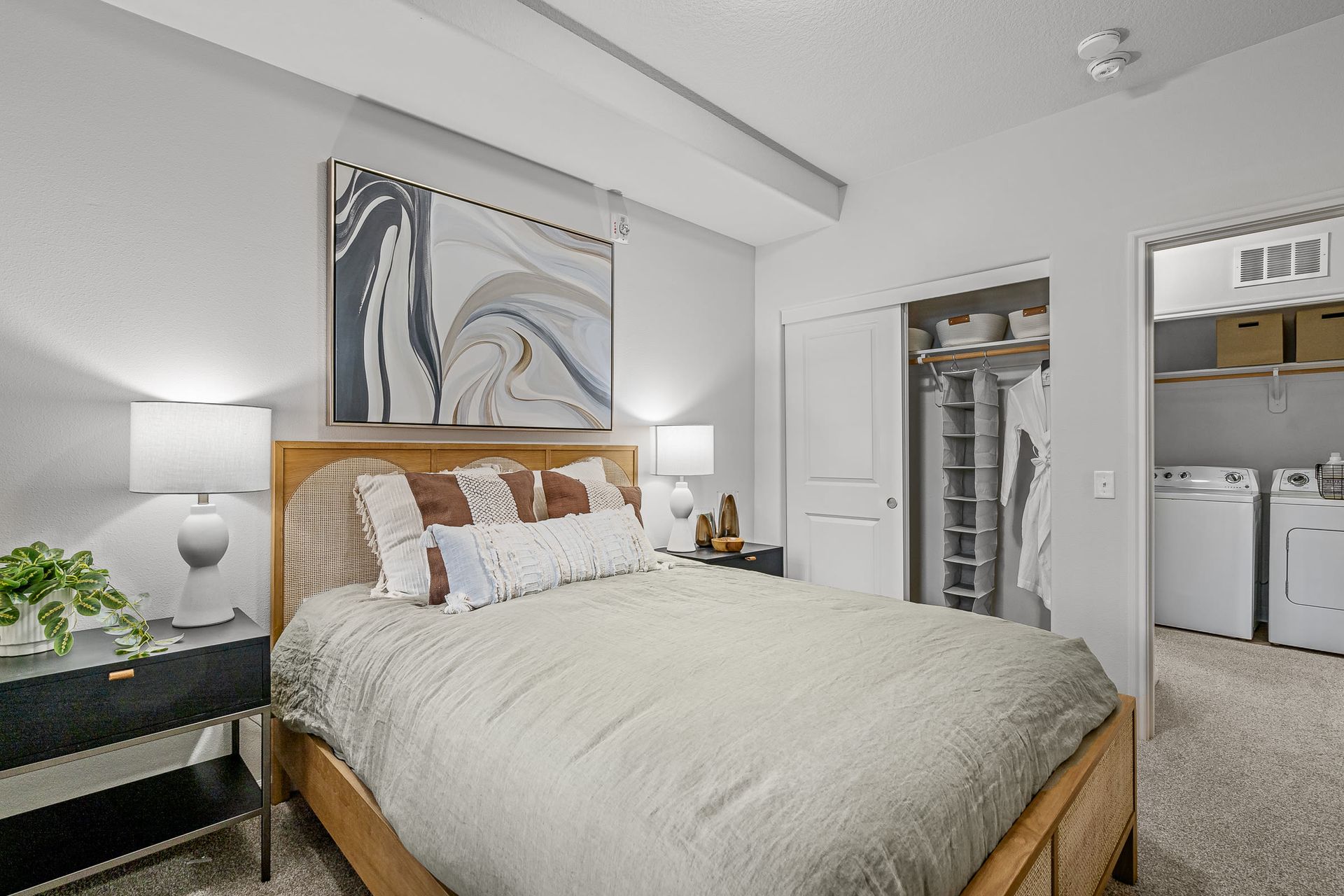 Bedroom with a wooden bed, two nightstands, art above, and a closet with washer/dryer.