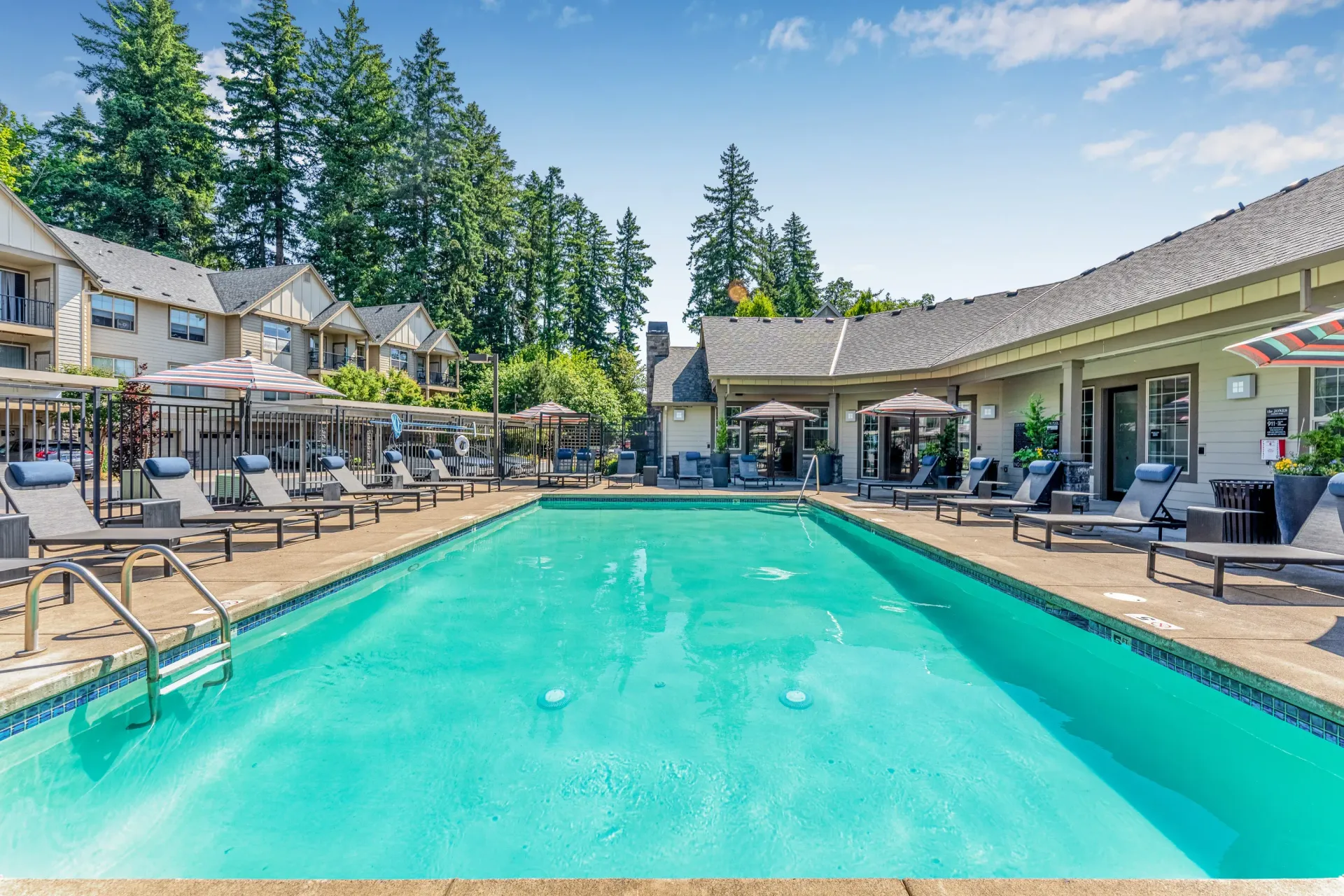 Outdoor apartment community pool with lounge chairs and umbrellas