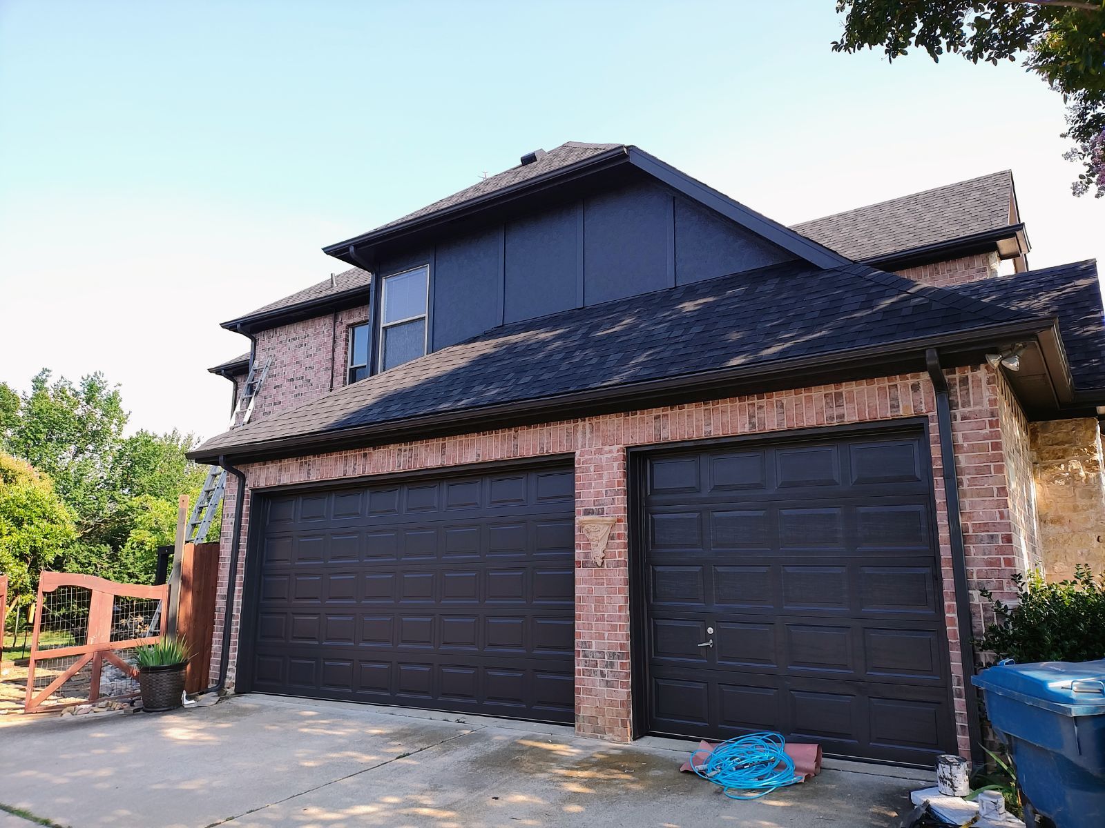 A large brick house with two black garage doors and a black roof.