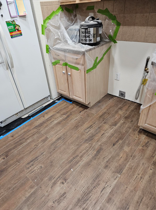 A kitchen with wooden floors , cabinets , a refrigerator and a sink.