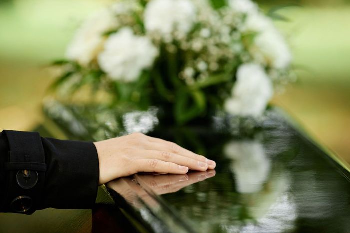 A Person Is Laying Their Hand on A Coffin at A Funeral.