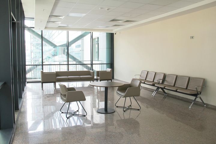 A waiting area with modern beige chairs, a circular table, and a long couch in a bright room with large glass windows.