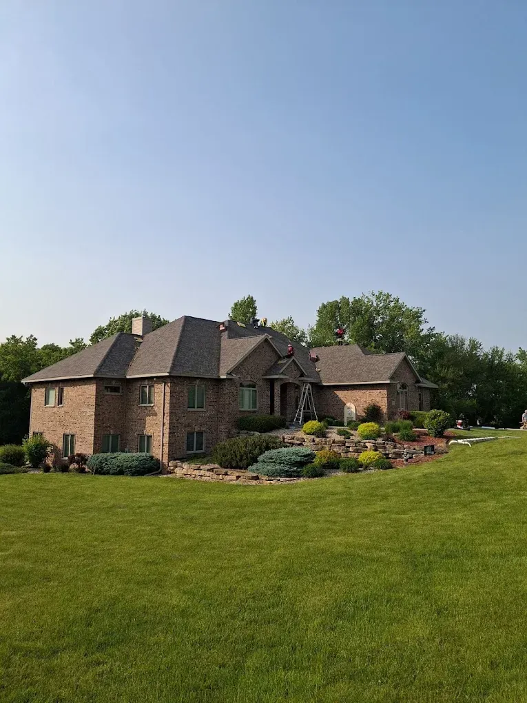 Brick house on a grassy hill with landscaped flower beds under a clear blue sky.