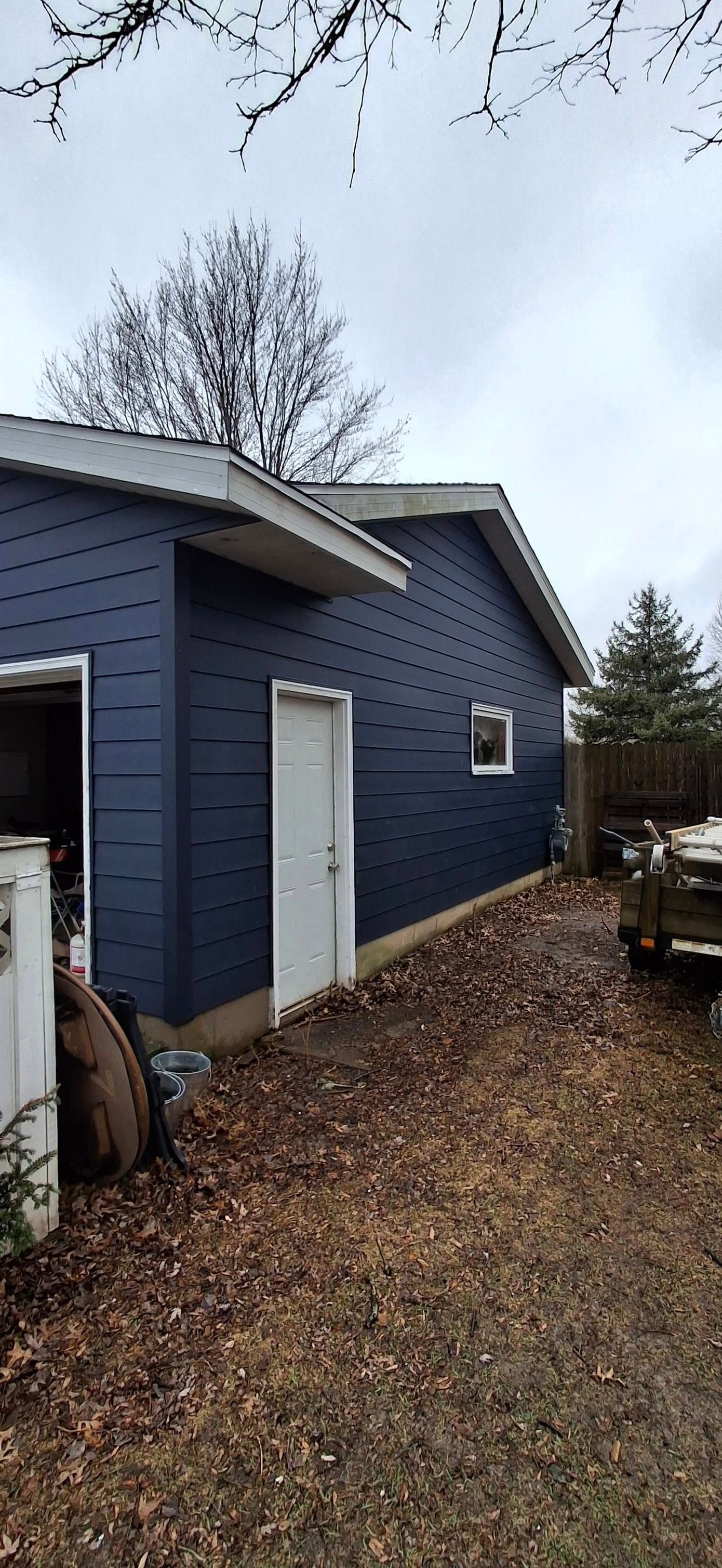 Blue-sided building with white trim and a white door in a yard covered in fall leaves.