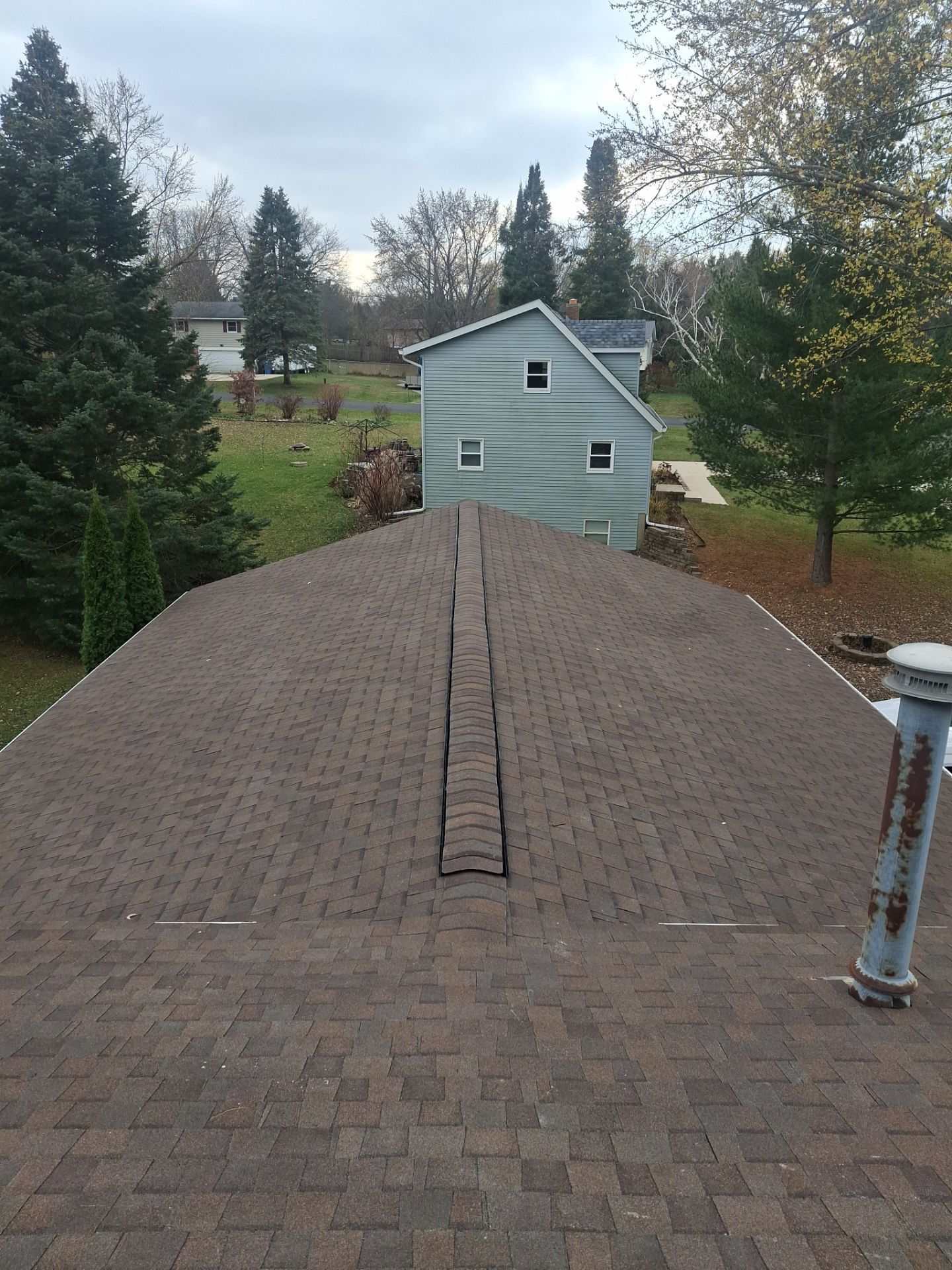 Brown shingle roof with a damaged center, a small green building, and trees in the background.