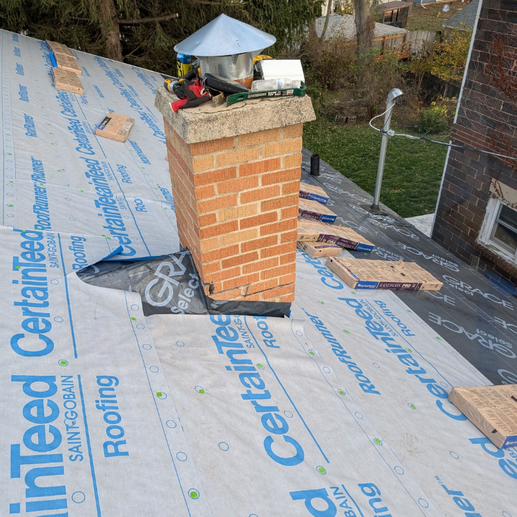 Rooftop with a brick chimney and a partially installed roofing membrane with CertainTeed logo.