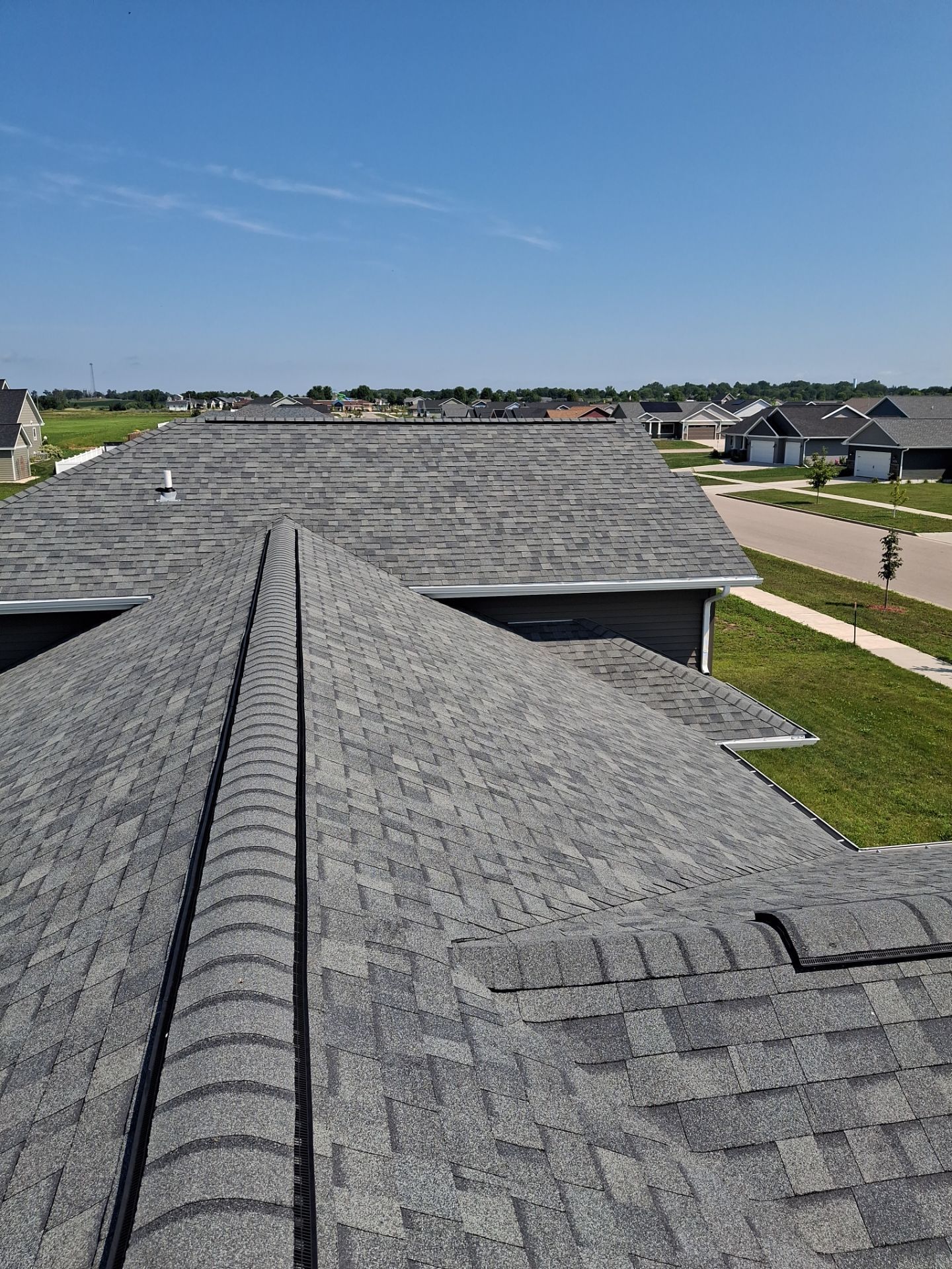 View of multiple gray shingled roofs on houses in a sunny residential neighborhood.