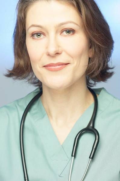 Woman in green scrubs with a stethoscope around her neck, smiling.
