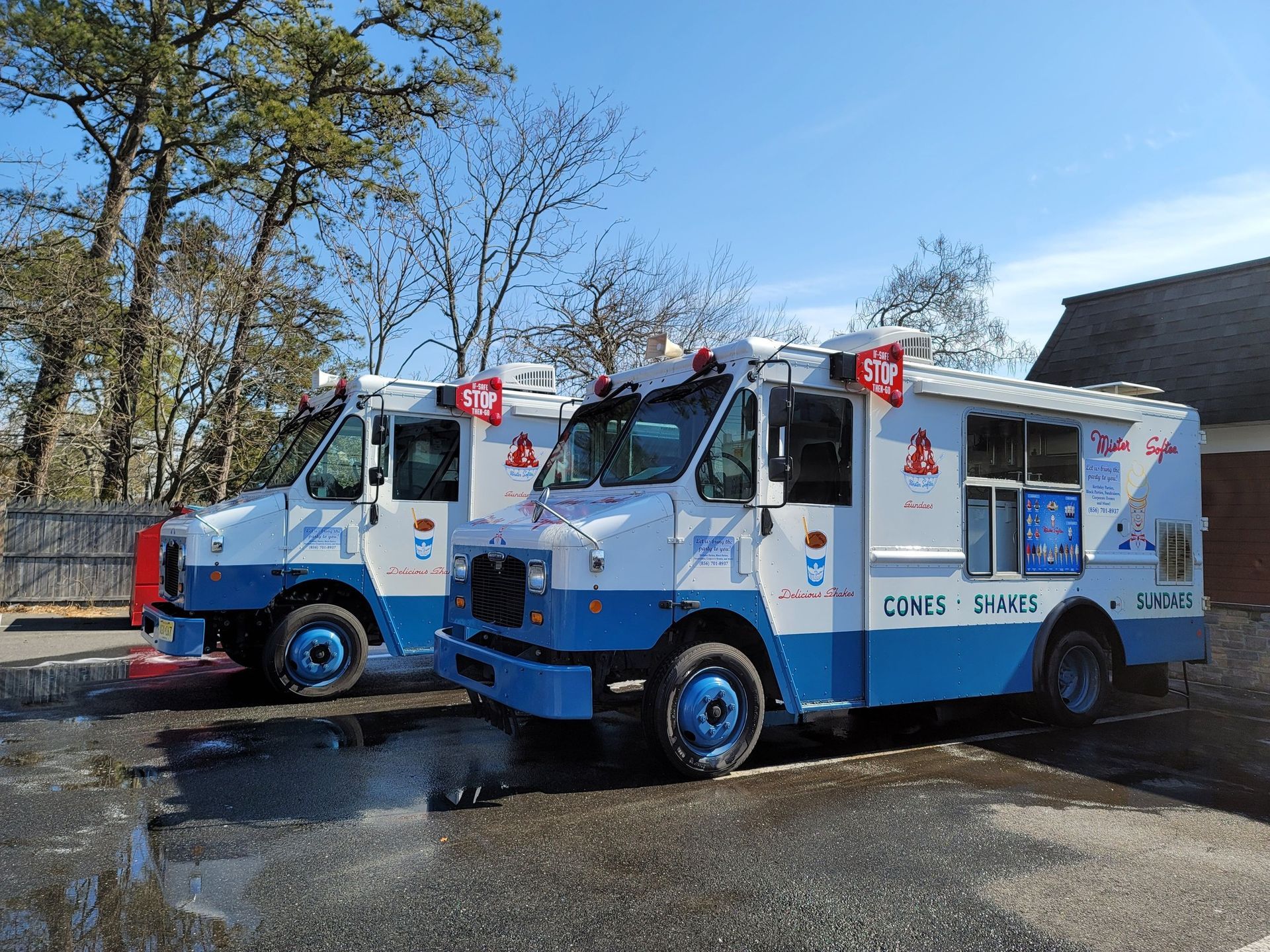 Two blue and white ice cream trucks parked outside on a sunny day.