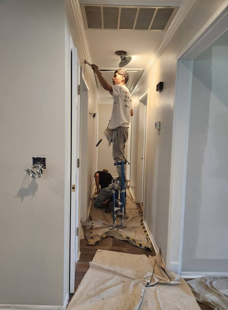 Two people painting a hallway. One on stilts painting the ceiling, the other on the floor.
