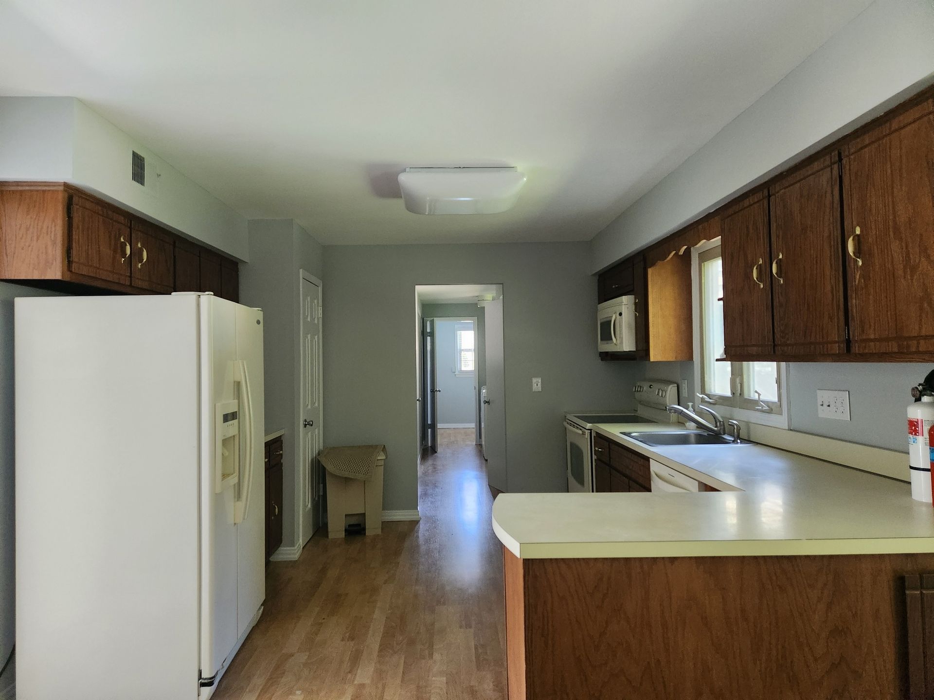 Kitchen with wooden cabinets, white appliances, gray walls, and a light-colored countertop.