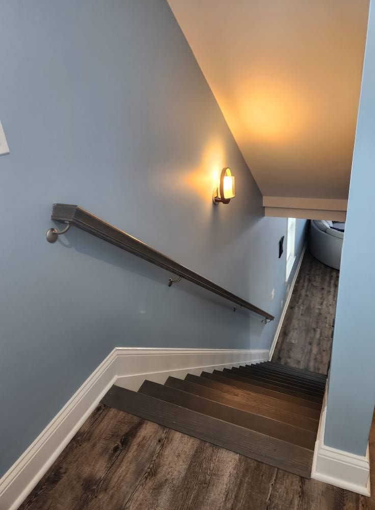 Staircase with gray steps and handrail, light blue walls, and a warm-toned wall sconce.