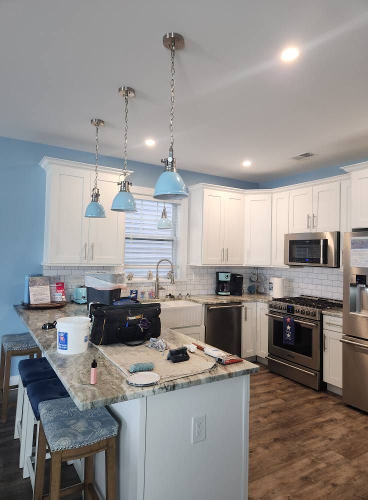 Kitchen with white cabinets, blue walls, a granite countertop island, and three blue pendant lights.