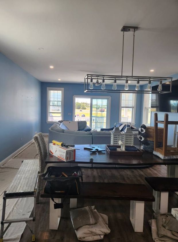 Interior of a dining area with a table, benches, and a blue wall. Natural light enters through windows.