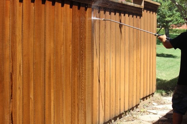 Person power washing a wooden fence, cleaning off dirt and debris.