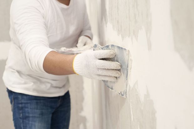 Person in gloves applying spackle to a wall with a putty knife.