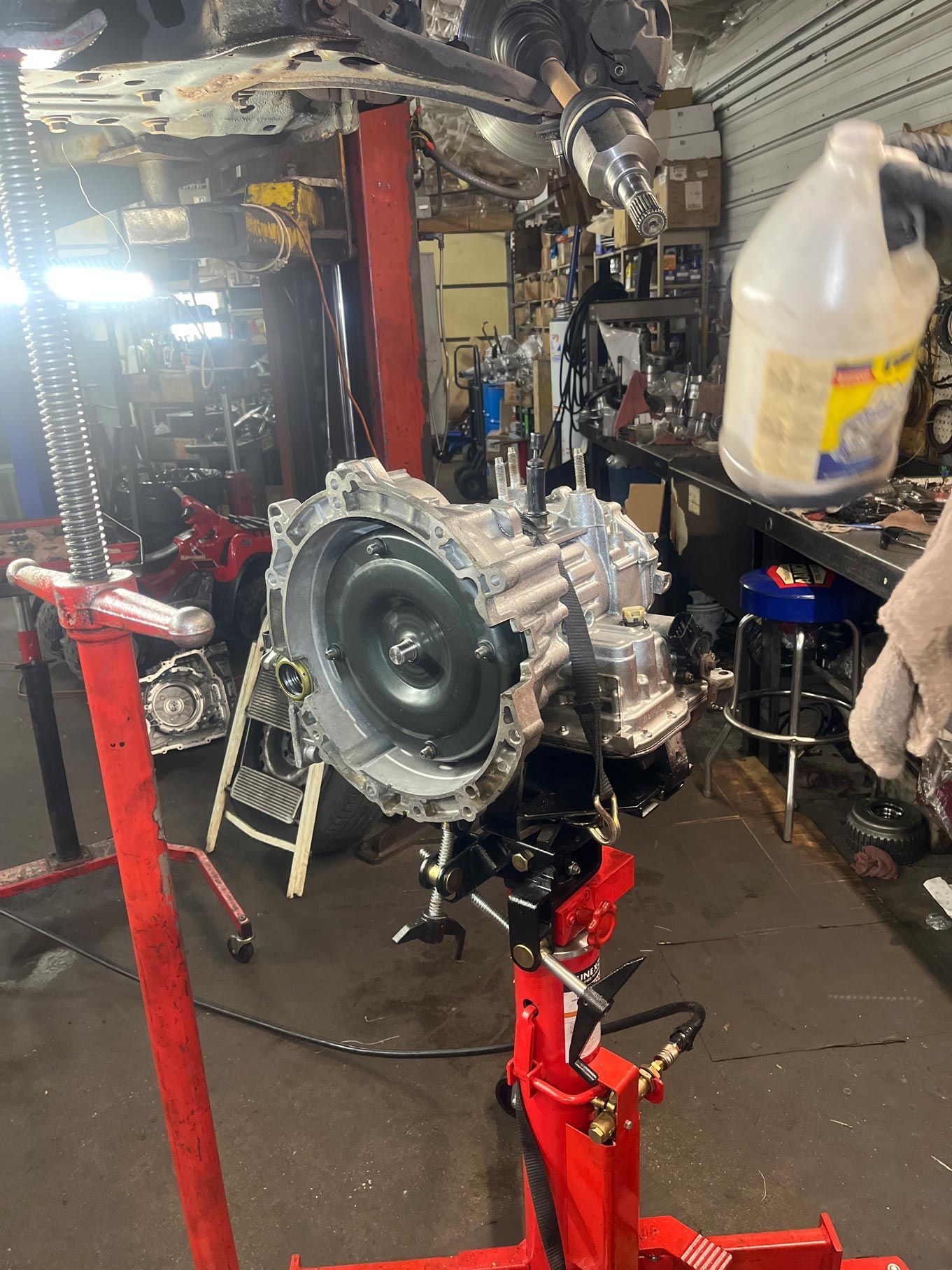 Transmission on a red lift in a cluttered auto shop.