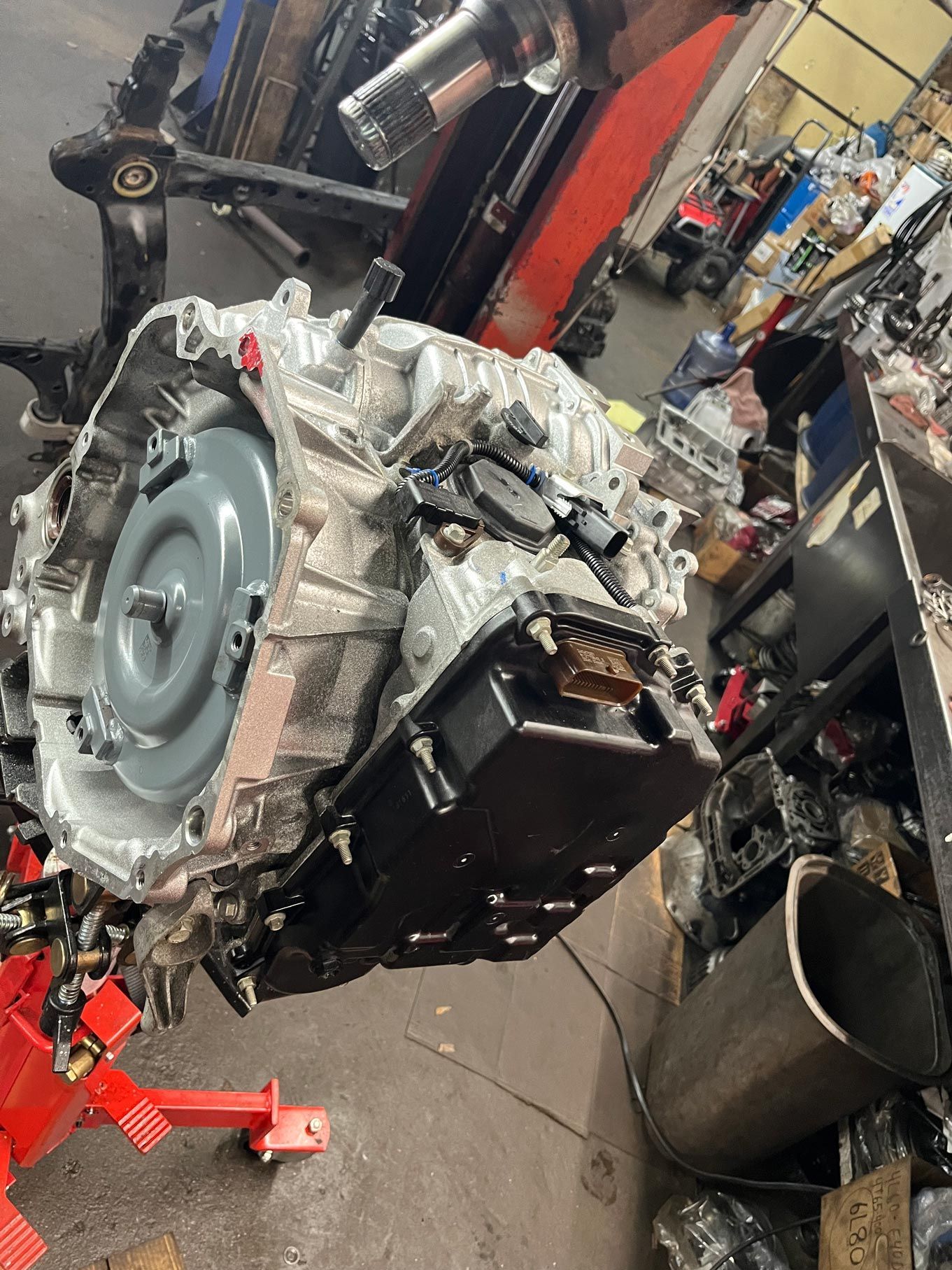 Transmission on a stand in a cluttered garage, showing the casing, fluid pan, and torque converter.