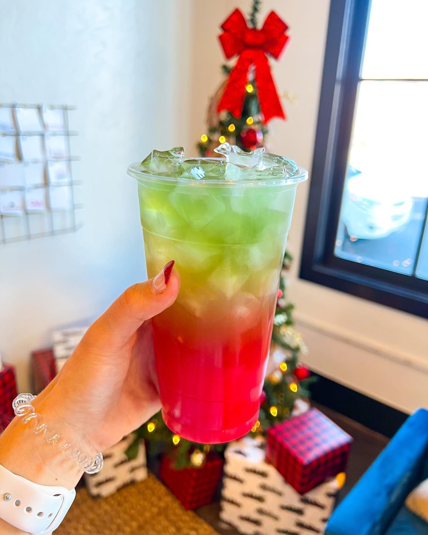 A person is holding a drink in front of a christmas tree.