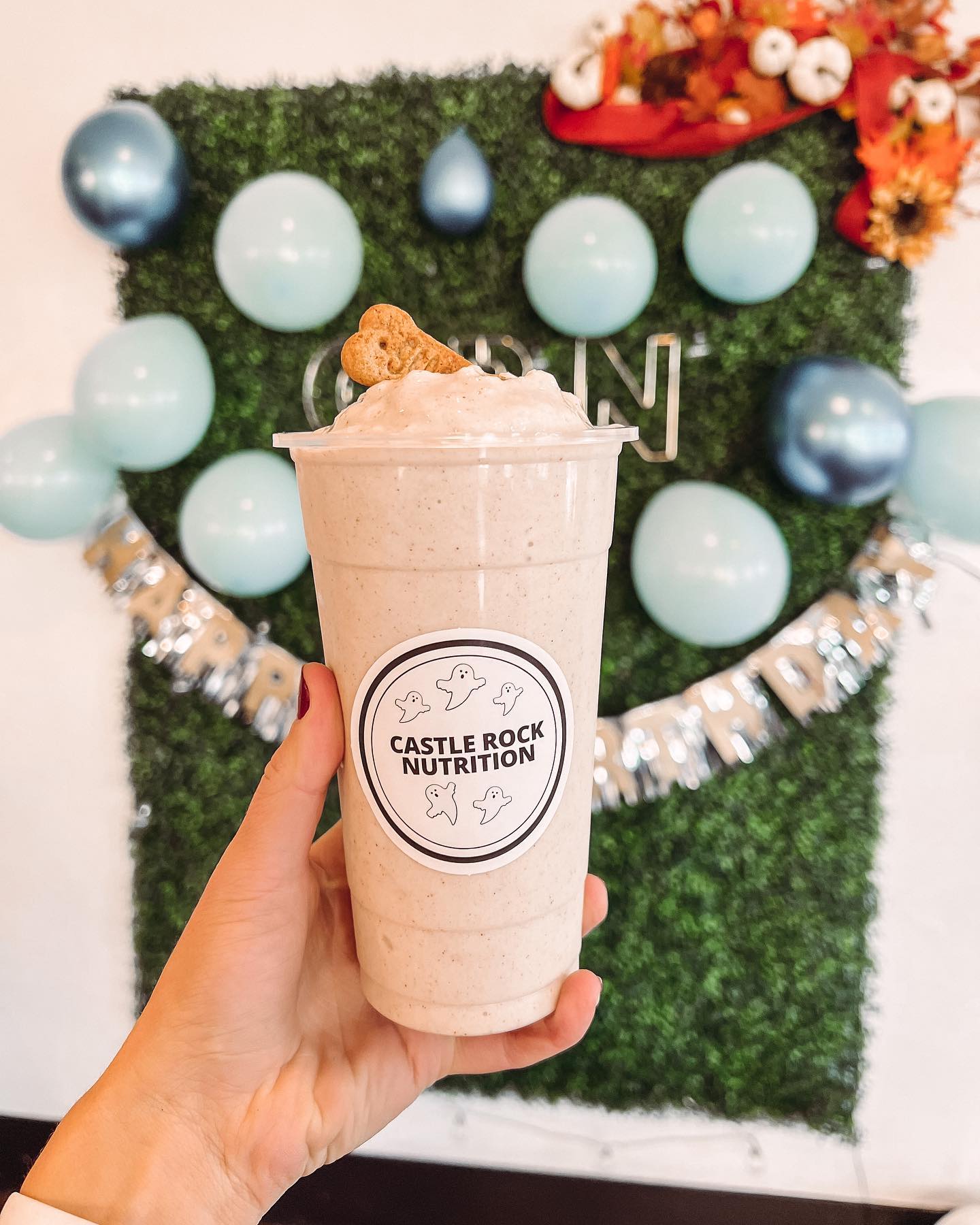 A person is holding a milkshake in front of a wall with balloons.