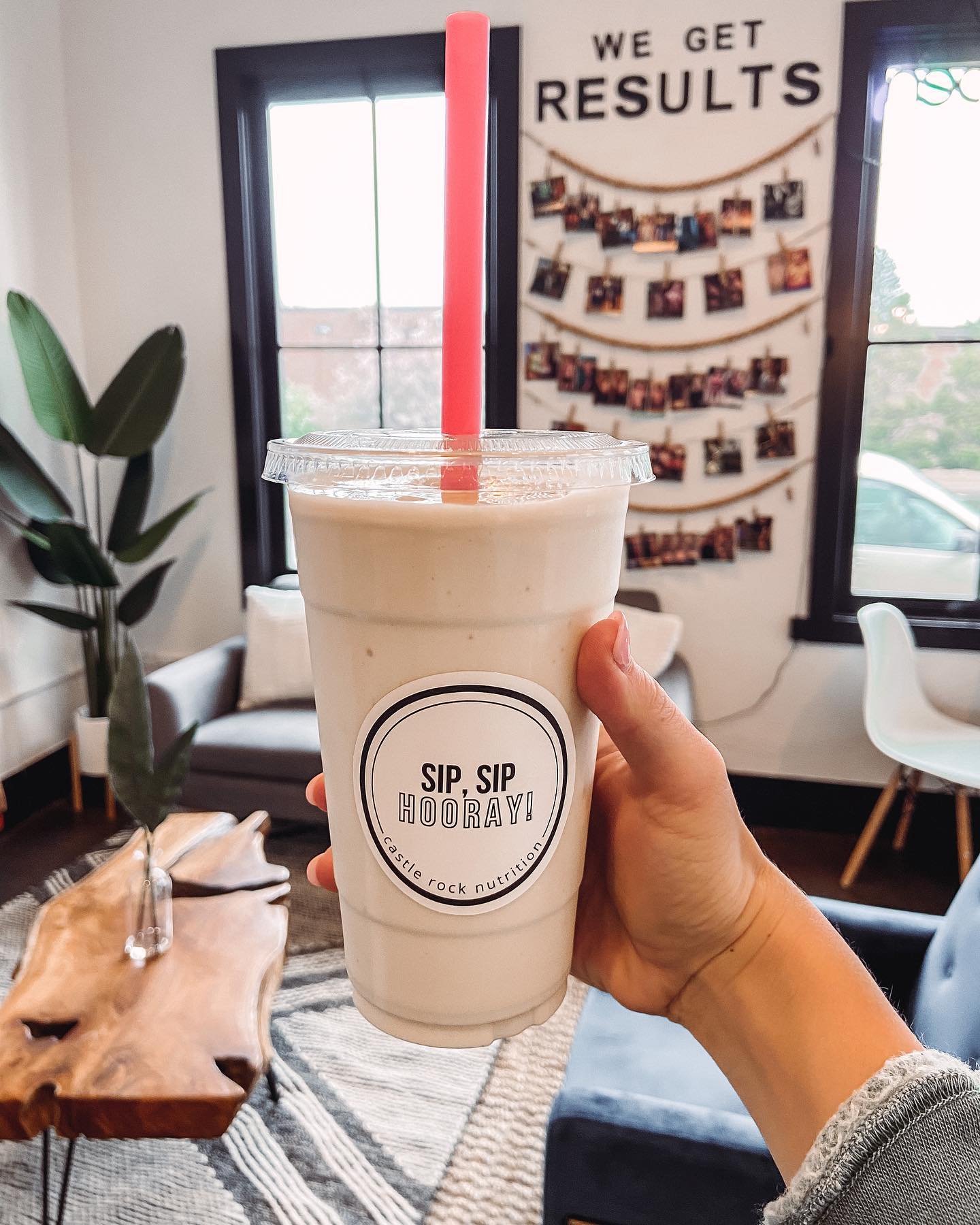 A person is holding a cup of milkshake in front of a sign that says we get results