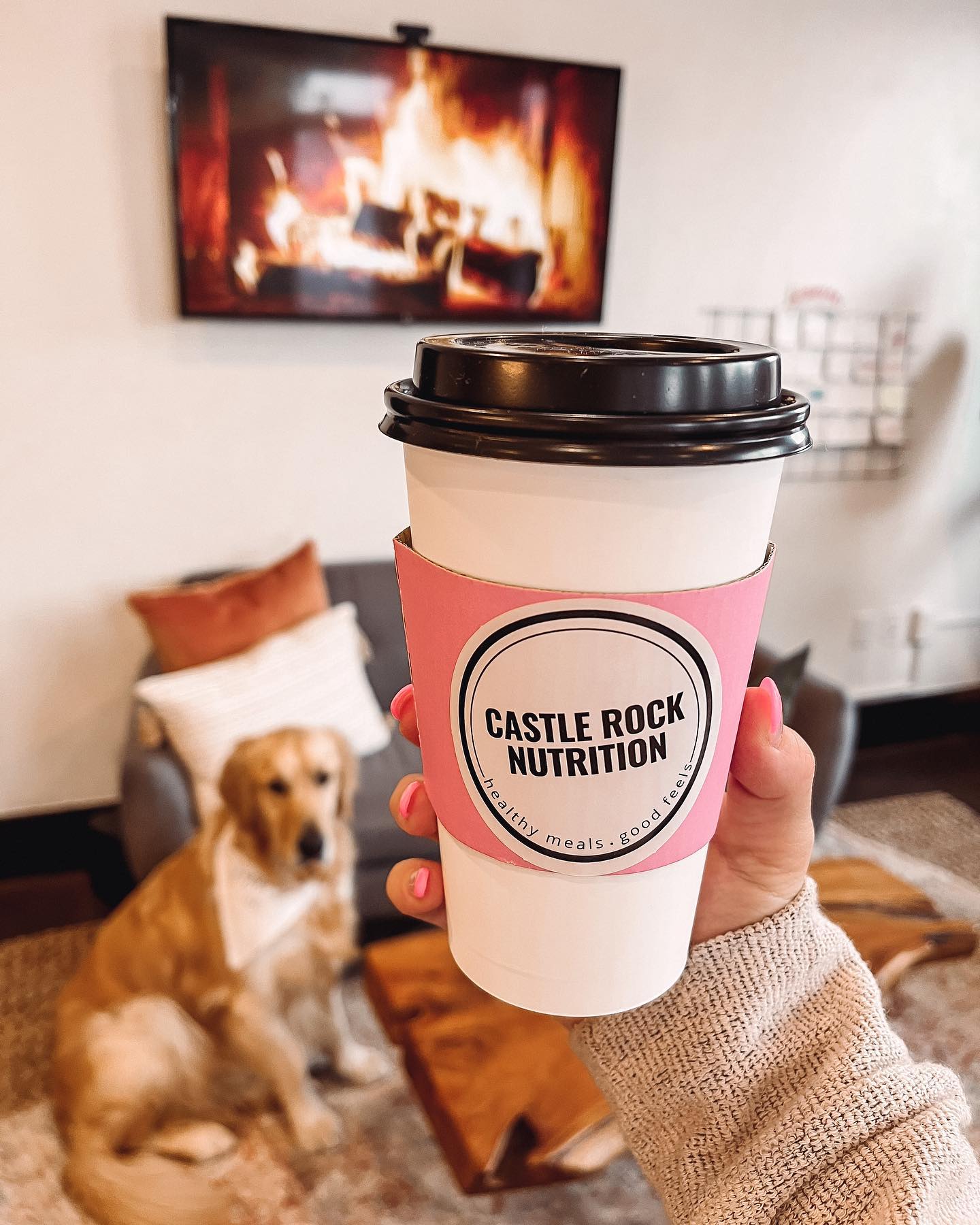 A person is holding a cup of coffee in front of a fireplace.
