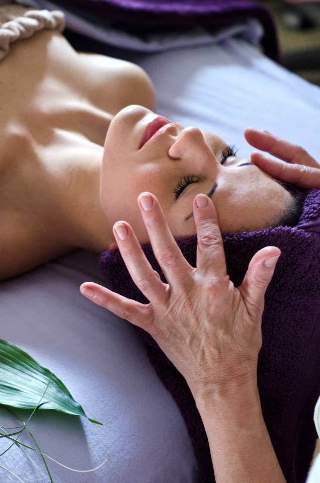 A woman is laying on a bed getting a facial massage.