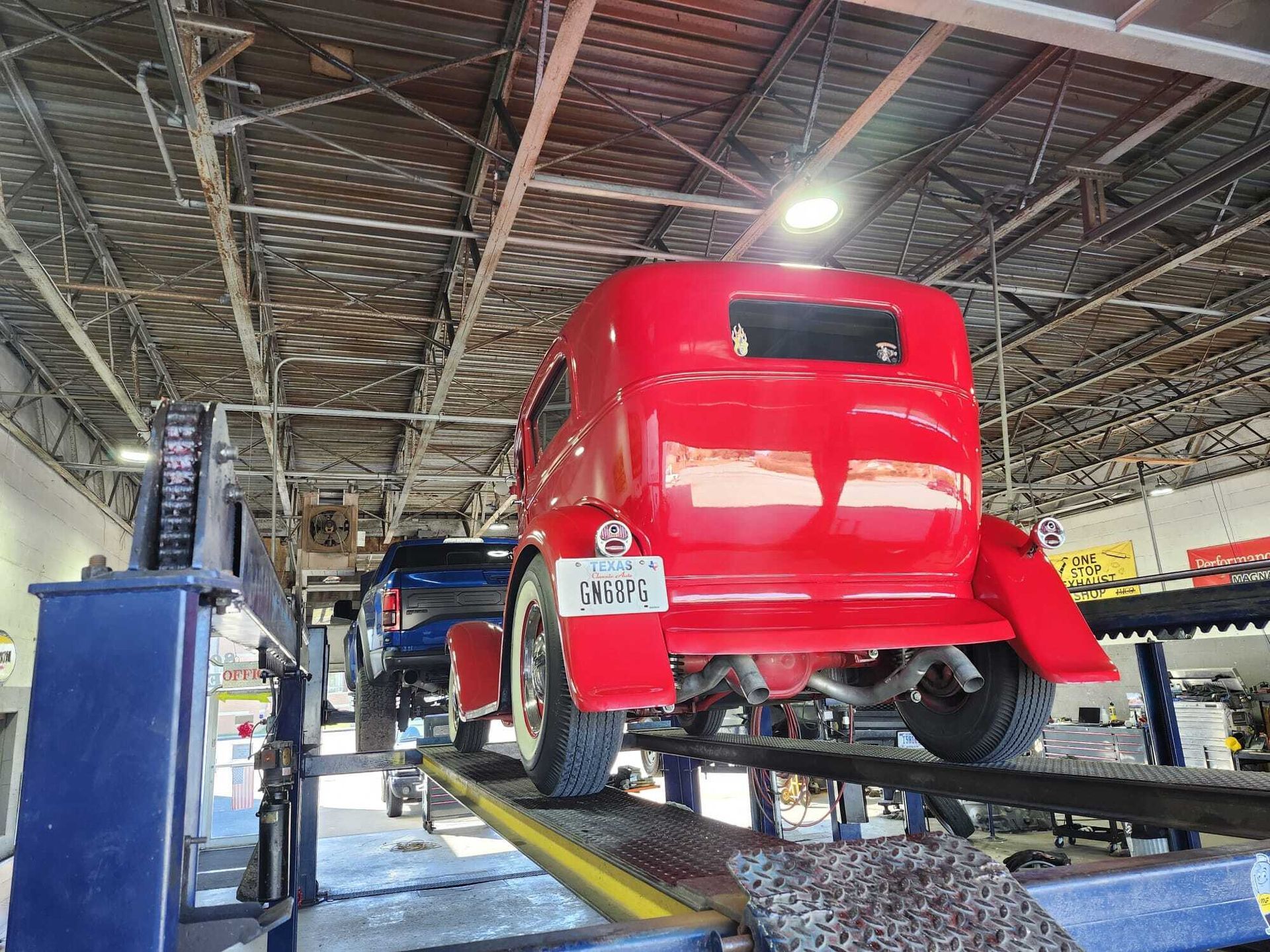 Red classic car on a lift inside a garage. Other vehicles and equipment are visible.| Garbs Automotive & Exhaust