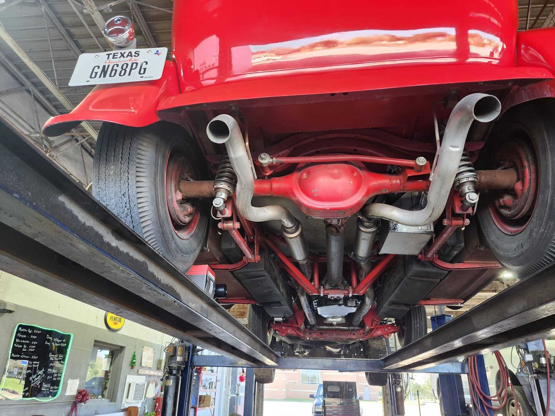 Underside view of a red classic car on a lift, showing suspension, exhaust, and license plate. Texas.| Garbs Automotive & Exhaust
