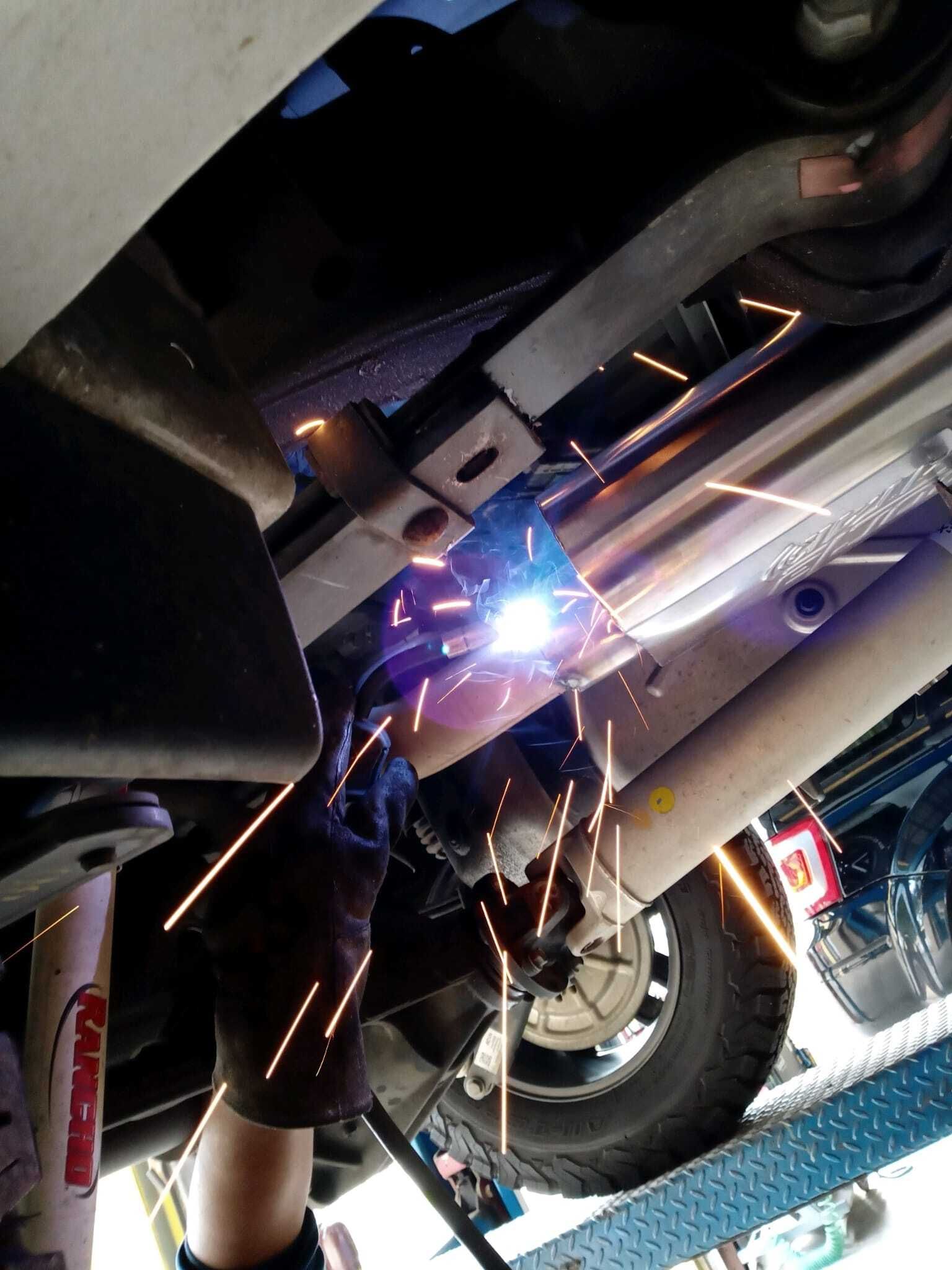 Person welding an exhaust pipe under a car, sparks flying.| Garbs Automotive & Exhaust