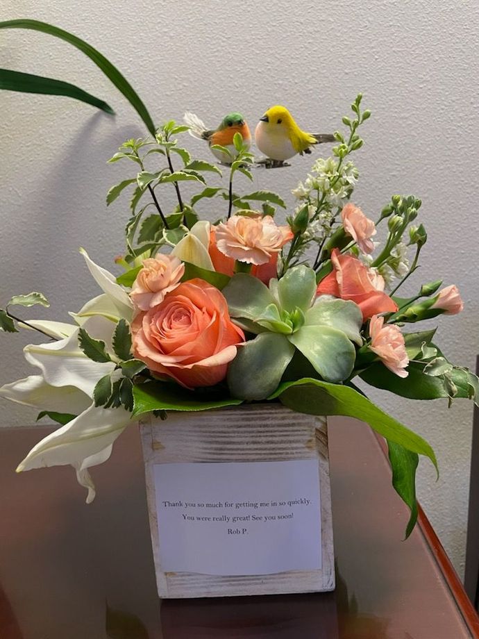 Floral arrangement in a white box with peach roses, greenery, and two small bird decorations
