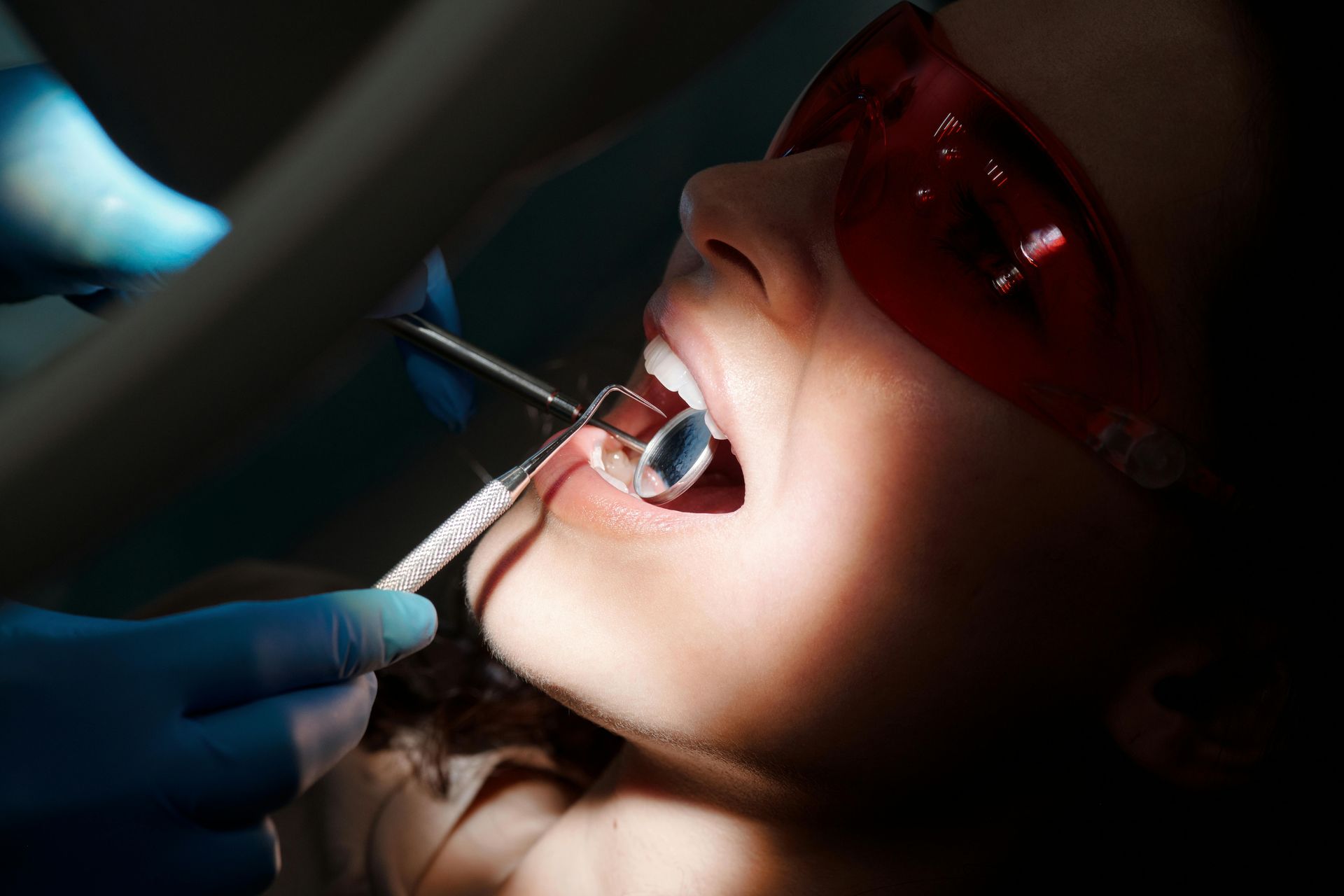 Dentist working on a patient’s open mouth with dental tools under bright exam light