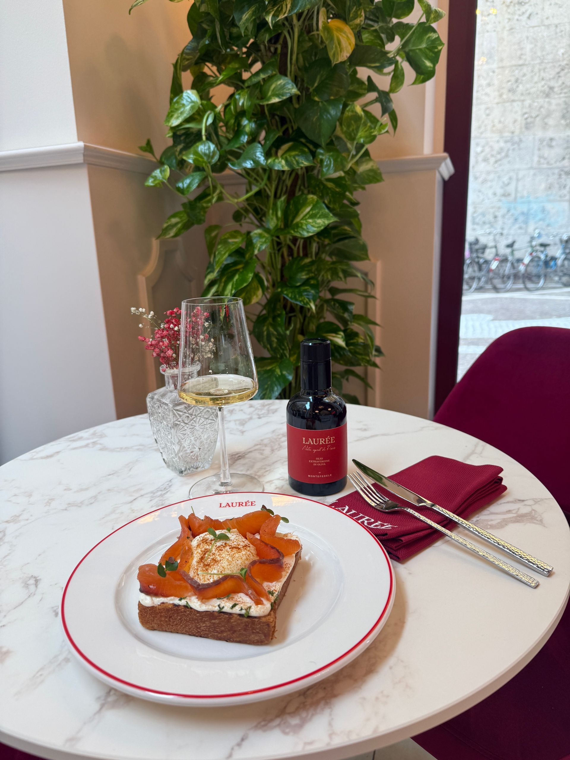 Una fetta di salmone tostato su un piatto bianco, con un bicchiere di vino bianco e una bottiglietta su un tavolo rotondo di marmo.