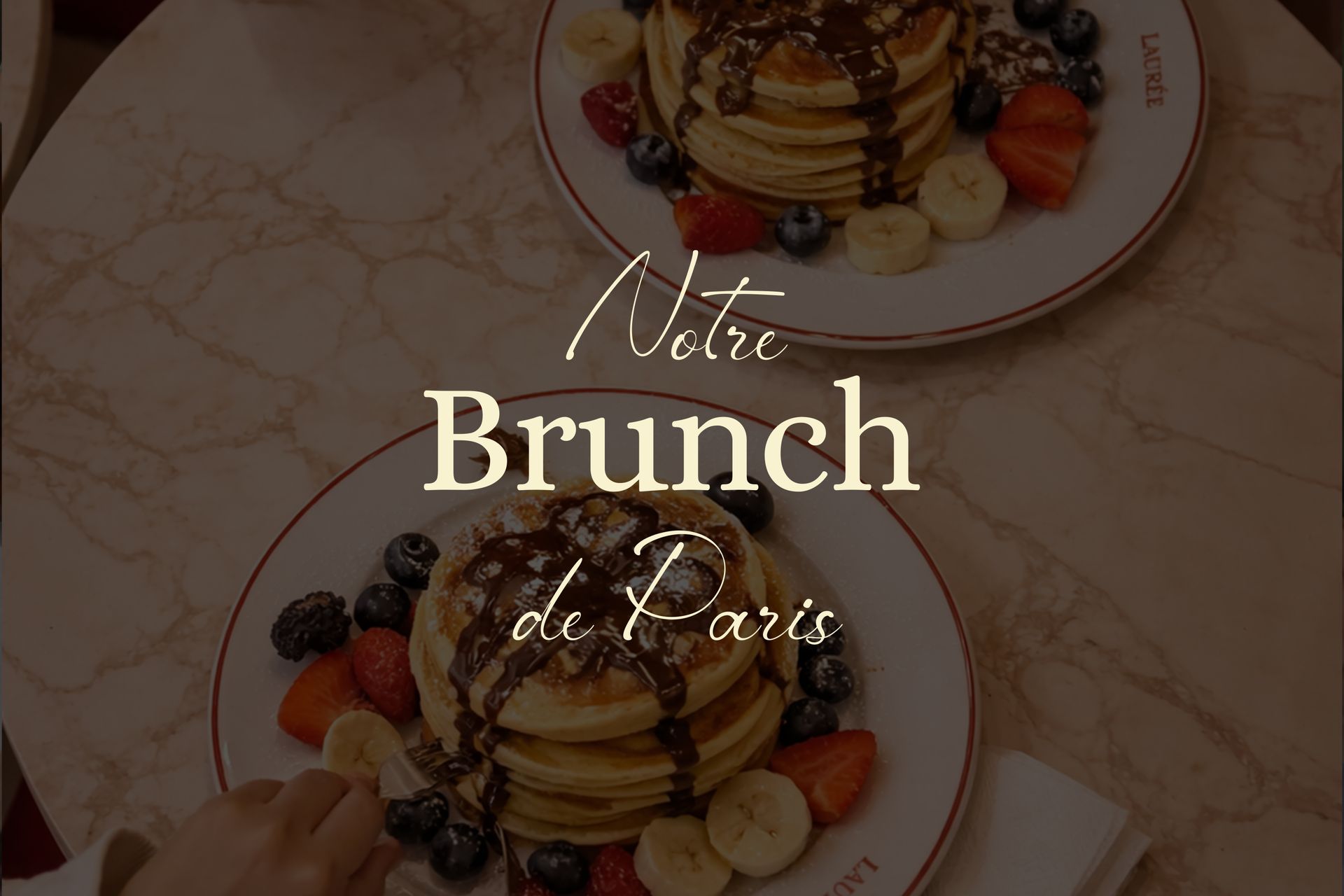 Due piatti di pancake guarniti con cioccolato e frutta fresca, disposti su un tavolo di marmo con la scritta "Notre Brunch de Paris".