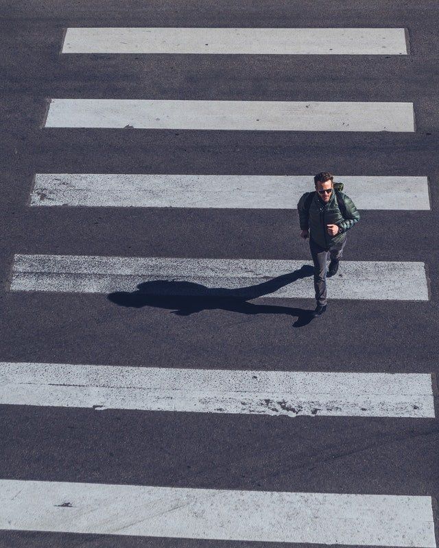 An image of a man wearing a puffy jacket and a backpack running across a crosswalk with thick white lines.