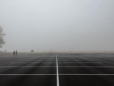 The first image is of an empty parking lot on a misty day at the beach. The second image is of freshly paved asphalt with a brightly painted double yellow line going down the center. The third image is of an asphalt paving machine as it rolls down the street during an asphalt patching and repair service..