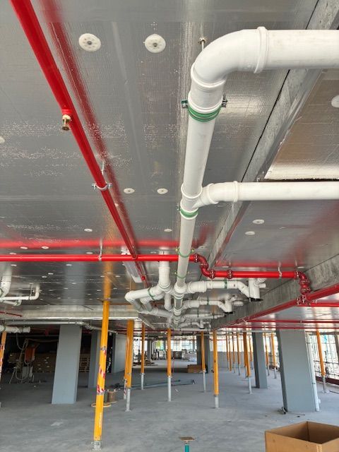 Plumber kneeling, working on sink pipes in a bathroom. Holding wrench, wearing blue work pants, white fixtures visible.