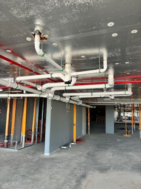 Plumber kneeling, working on sink pipes in a bathroom. Holding wrench, wearing blue work pants, white fixtures visible.