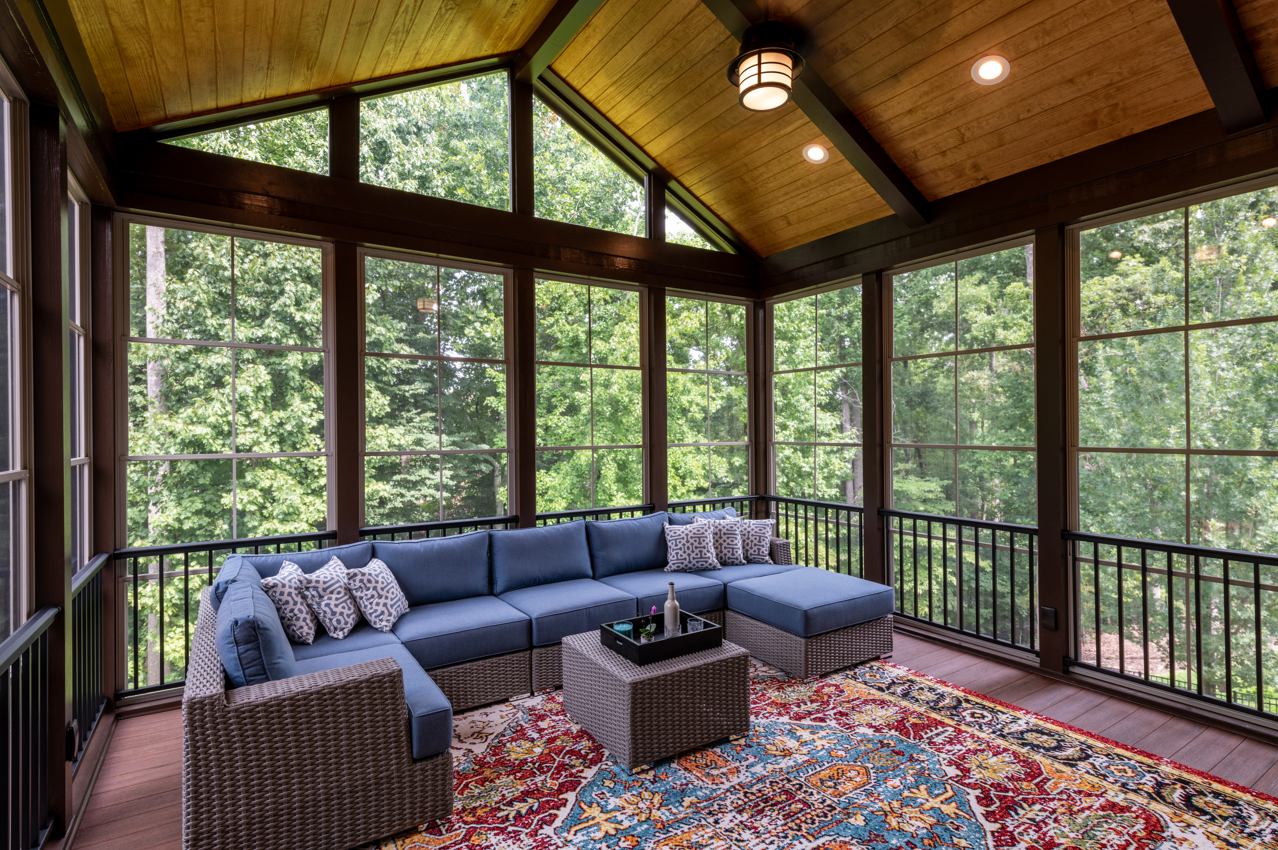 Screened porch with blue sectional, patterned rug, and surrounding forest.