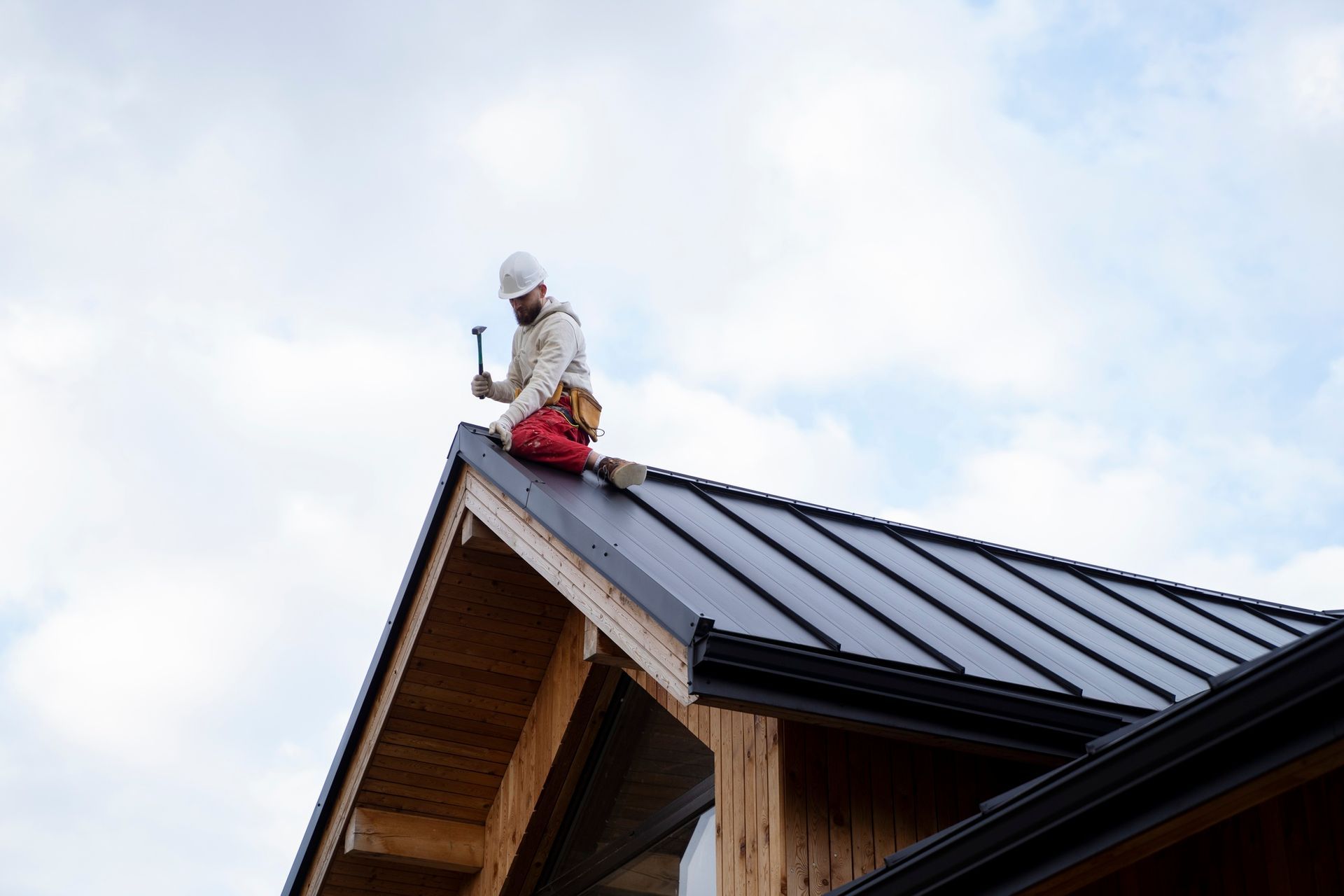 A man is kneeling on the roof of a house holding a hammer.