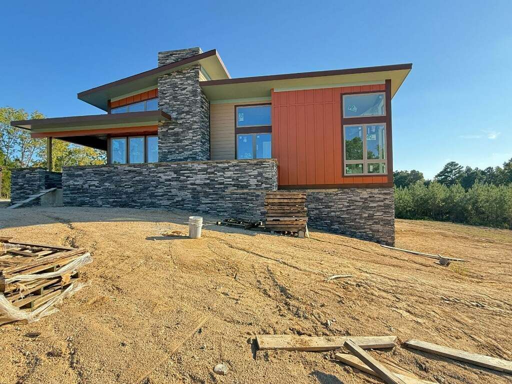 Modern home under construction with stone and orange siding, large windows, and a flat roof.