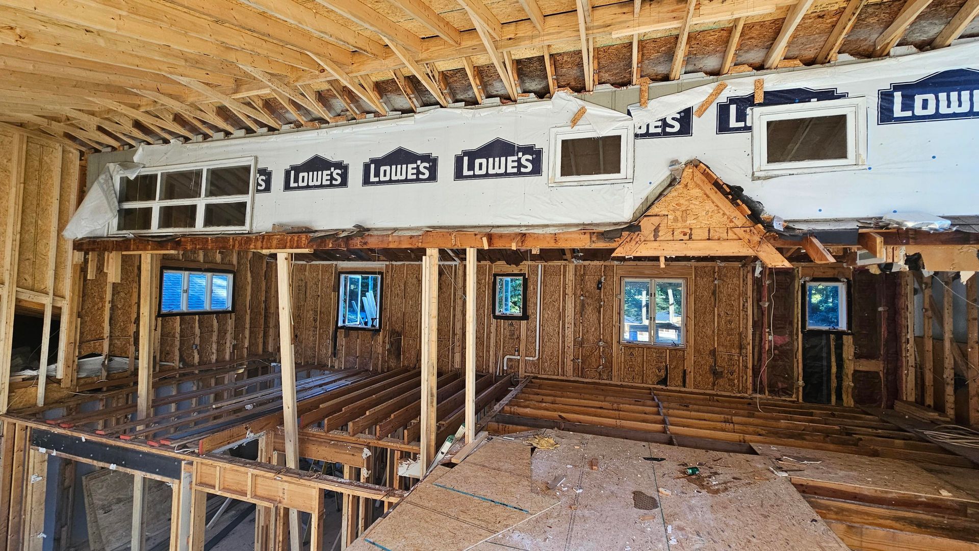 Interior of a building under construction, revealing wooden framing and exposed walls with windows.