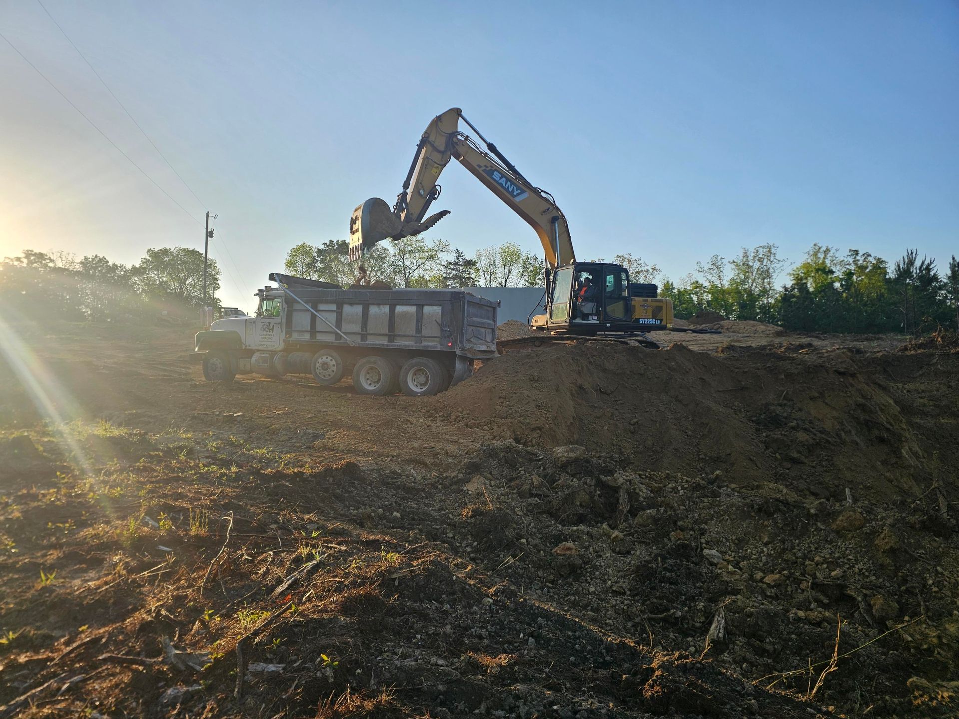 Excavator loading dirt into dump truck on construction site under a blue sky.